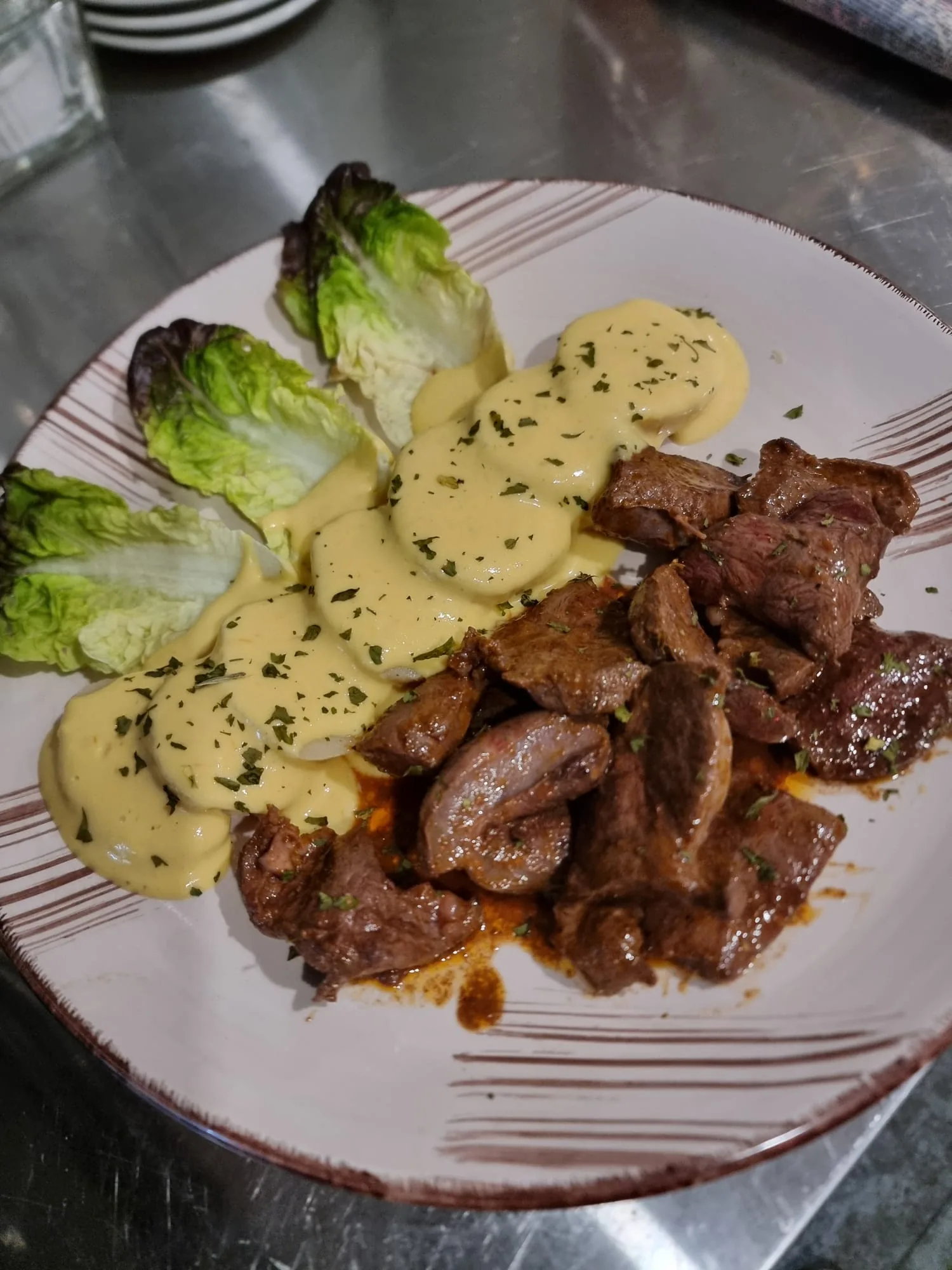 Anticucho peruano de Marquina's: trozos de carne salteada con salsa, acompañados de papa a la huancaína y hojas de lechuga, en plato blanco