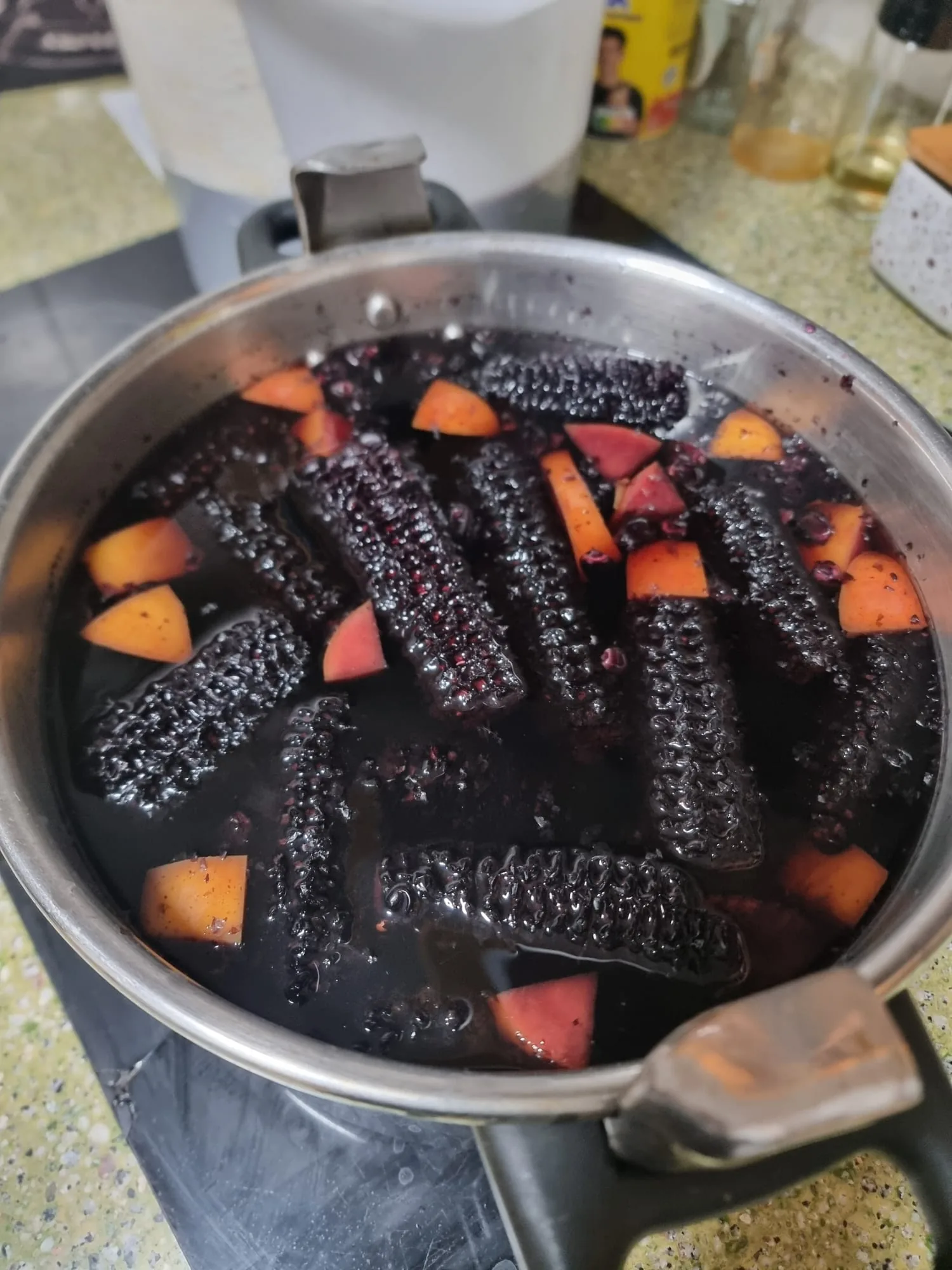 Chicha morada en preparación: mazorcas de maíz morado y trozos de fruta cociendo en una olla de acero en la cocina de Marquina's
