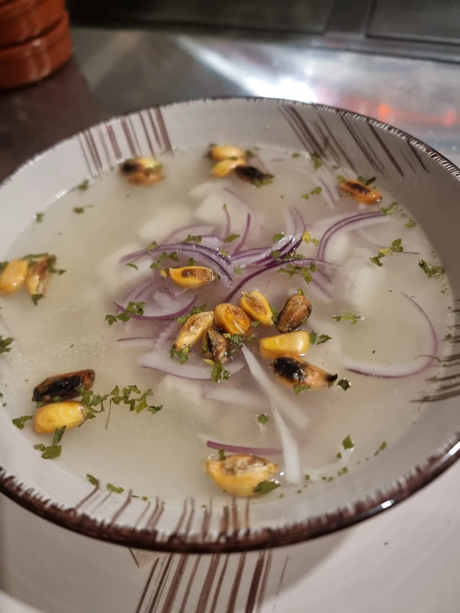 Chilcano de pescado de Marquina's: caldo claro con trozos de pescado, cebolla morada en tiras y maíz cancha, servido en cuenco blanco