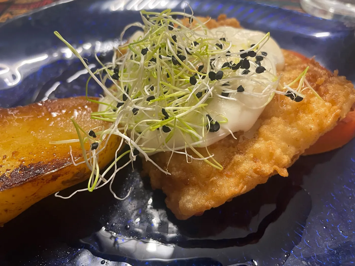Filete rebozado con salsa blanca y brotes, junto a una tajada de plátano frito en plato azul