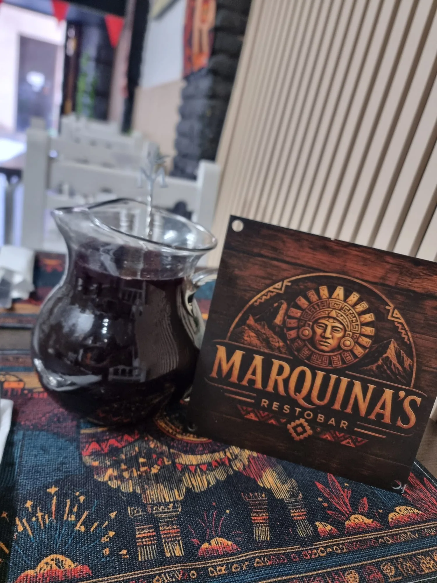 Jarra de vidrio con chicha morada servida, sobre mantel de motivos andinos, en el salón de Marquina's