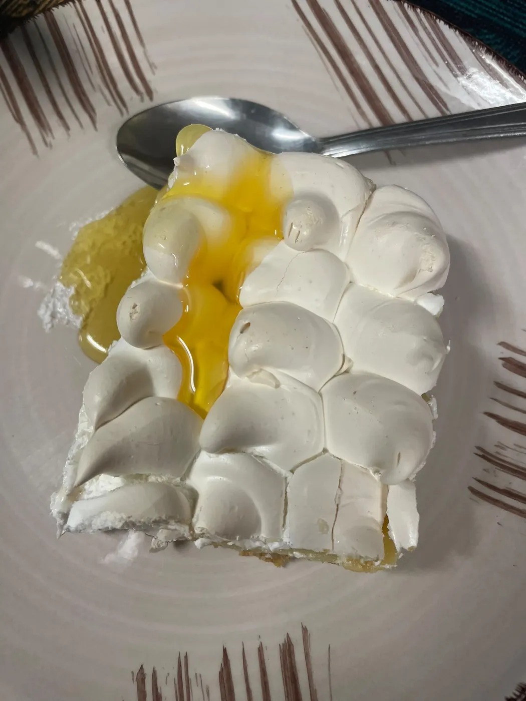 Porción de postre cubierta de merengue con un almíbar amarillo por encima