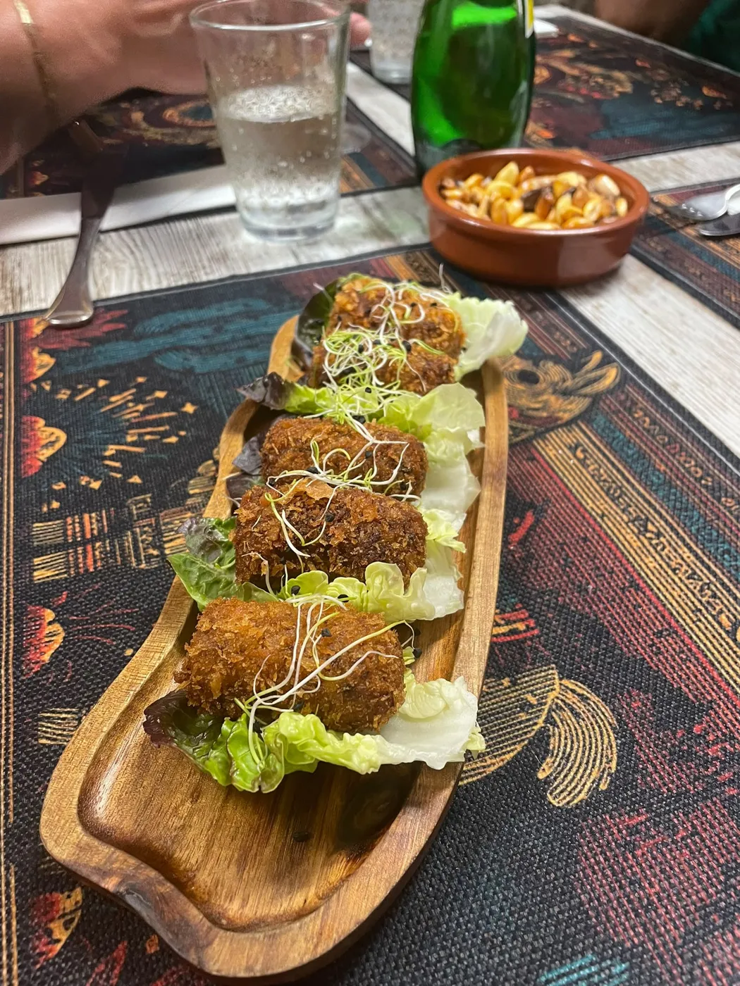Bocados rebozados y dorados sobre hojas de lechuga, con brotes, en una bandeja de madera