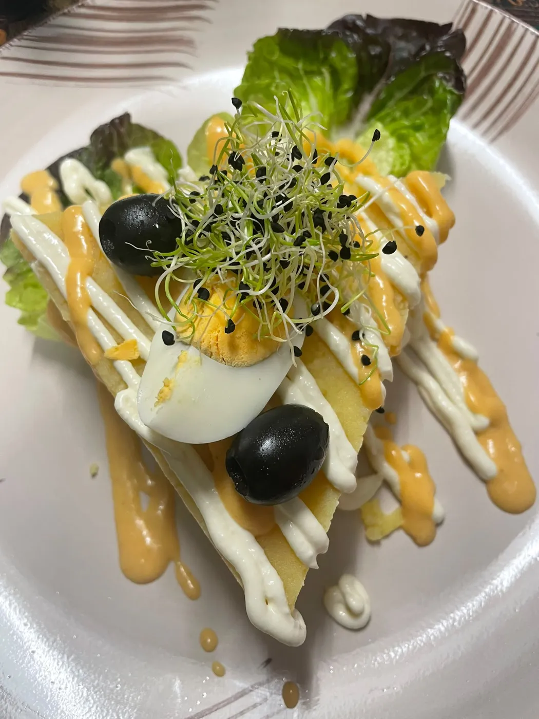 Capas de puré de patata amarilla con huevo duro, aceitunas negras, salsas y brotes sobre lechuga